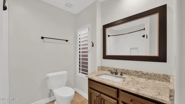 a bathroom with a granite countertop sink vanity mirror and toilet