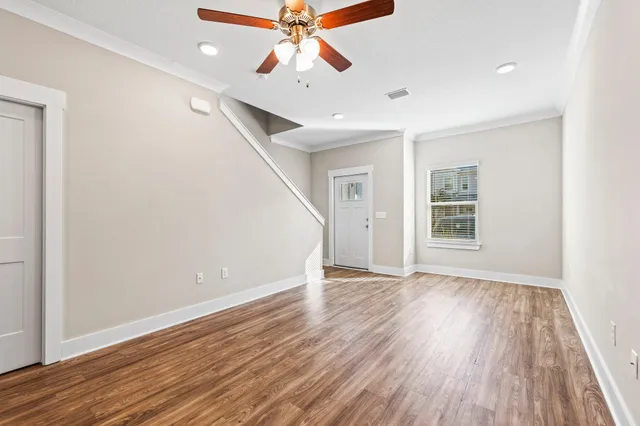 an empty room with wooden floor chandelier fan and windows