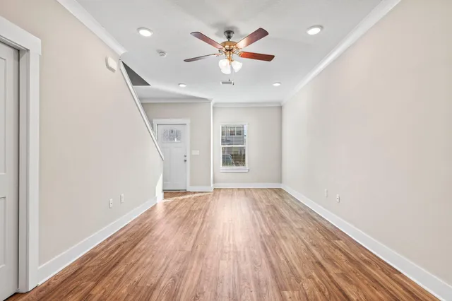 an empty room with wooden floor ceiling fan and windows