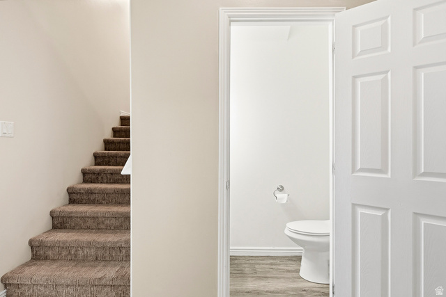 1177 Northfield Road, Unit 26 Cedar City, UT 84721 - Photo 17 of 45 Carpeted stairway with a white light switch and a partial view of a bathroom featuring wood-finish flooring, white baseboards, and a white toilet