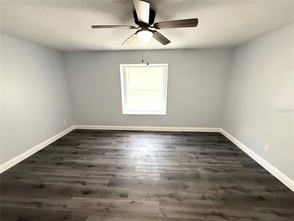 an empty room with wooden floor ceiling fan and windows