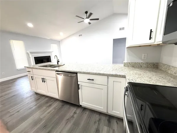 a kitchen with stainless steel appliances white cabinets a sink a stove a microwave and wooden floors