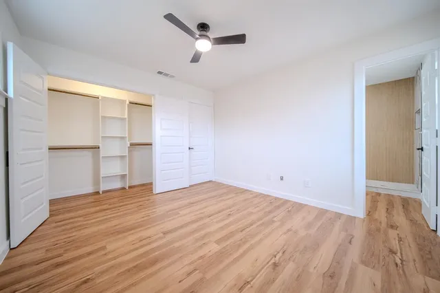 an empty room with wooden floor ceiling fan and windows