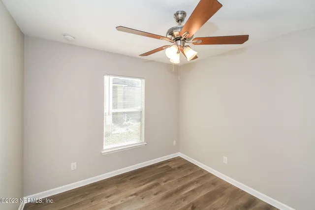 an empty room with wooden floor fan and windows