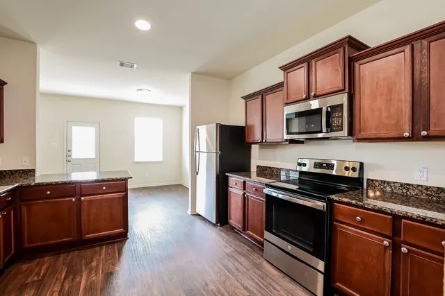 a kitchen with stainless steel appliances granite countertop a stove a sink dishwasher a microwave oven and a refrigerator with wooden floor