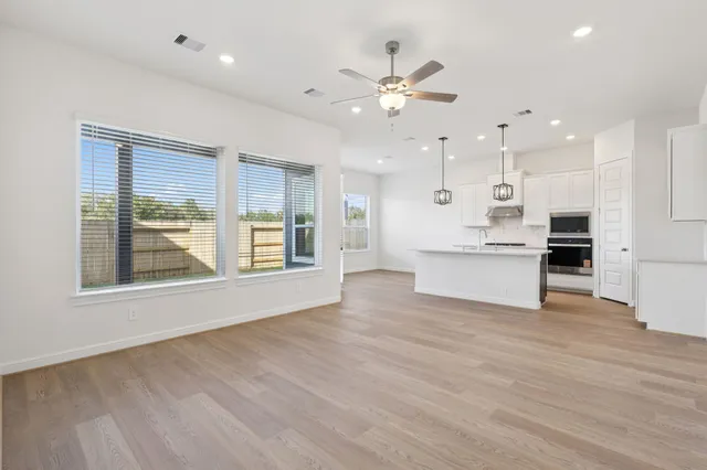 a view of an empty room with kitchen and window