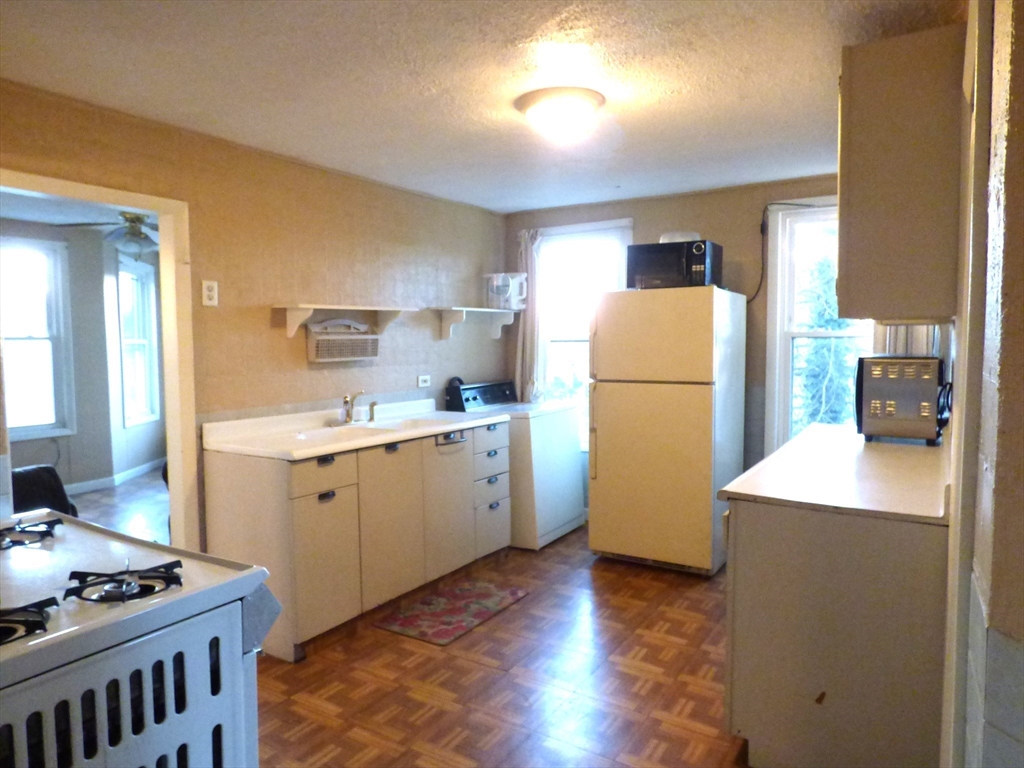 298 Main Street Springfield, MA 01151 - Photo 29 of 40 a kitchen with a refrigerator a stove a sink and a dining table with wooden floor