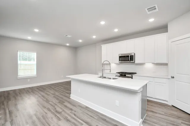 a kitchen with stainless steel appliances a microwave a sink a stove a microwave a center island and a window