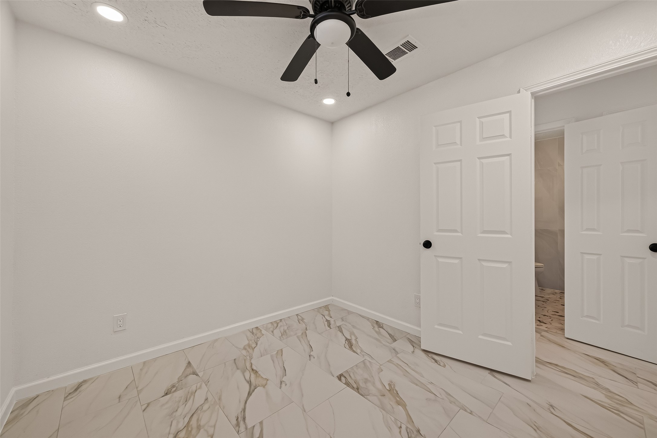 16619 Tibet Road Friendswood, TX 77546 - Photo 24 of 29 This room features clean white walls, marble-patterned tile flooring, and a ceiling fan with light. A partially open door reveals an adjacent space, offering a modern and neutral setting.
