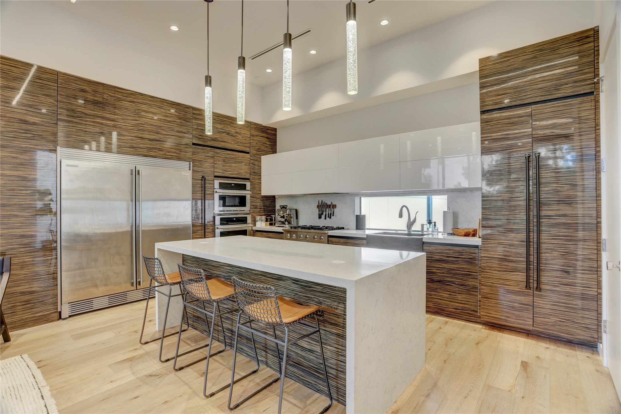 1807 Indiana Street Houston, TX 77006 - Photo 13 of 35 Kitchen Detail: Alternate kitchen view highlighting the seamless panel-ready refrigerator and wall ovens, a contemporary stone-topped waterfall island, custom modern cylinder pendant lights, and extensive high-gloss cabinetry storage.