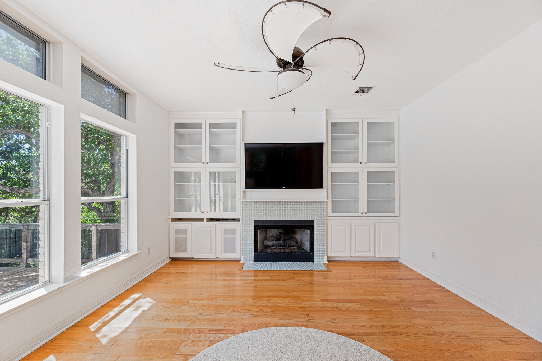 304 River Down Road Georgetown, TX 78628 - Photo 4 of 22 Living area featuring a fireplace with a dark stone hearth, built-in cabinetry with glass-front uppers, wood-finish flooring, a ceiling fan, and large windows