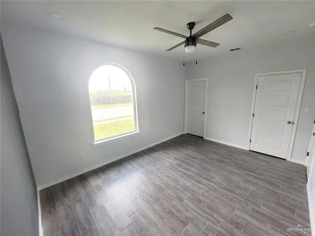 an empty room with wooden floor chandelier fan and windows