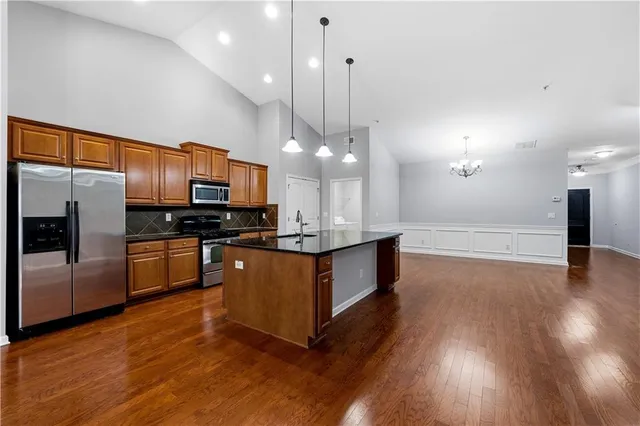 a kitchen with stainless steel appliances kitchen island granite countertop a refrigerator a oven a sink and a wooden floor