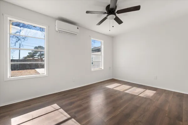 an empty room with wooden floor fan and windows