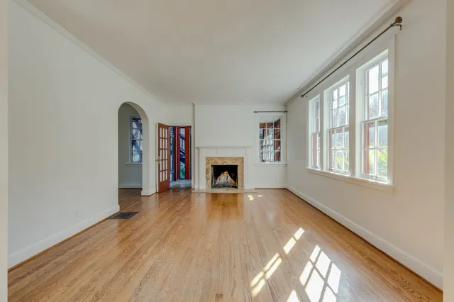 an empty room with wooden floor fireplace and windows
