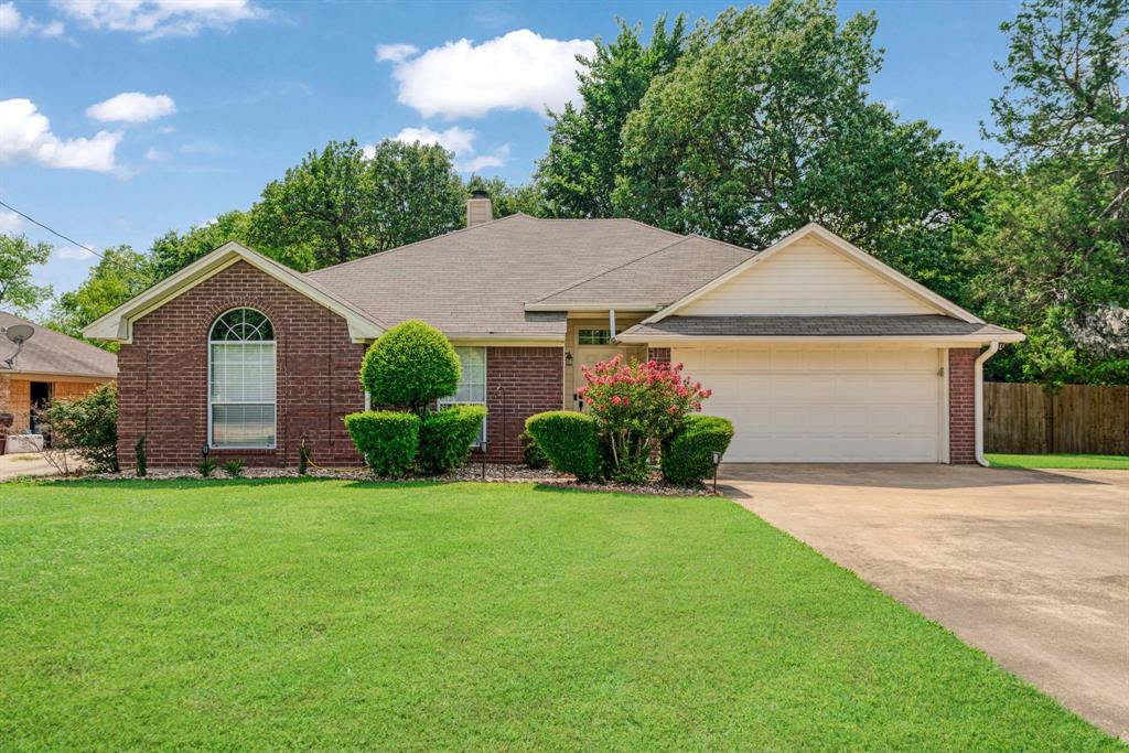 Single story home featuring driveway, brick siding, an attached garage, a chimney, and a shingled roof