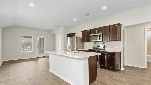 a kitchen with stainless steel appliances granite countertop a stove top oven a sink dishwasher and a refrigerator with wooden floor