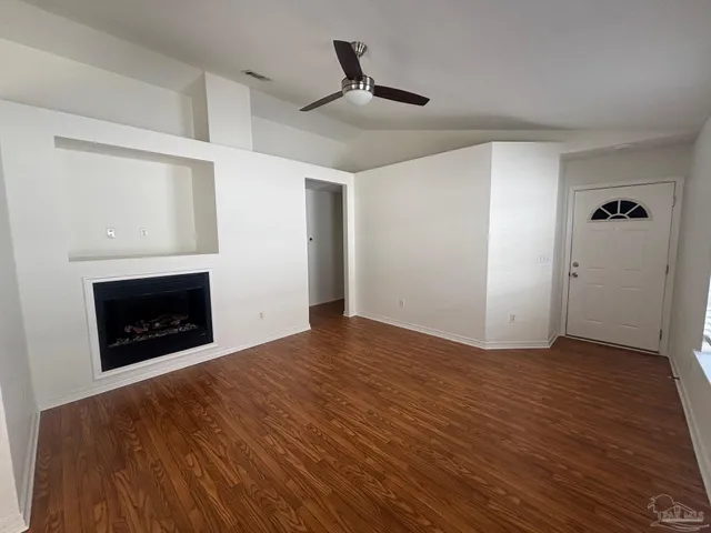 a view of an empty room with wooden floor fireplace and a window