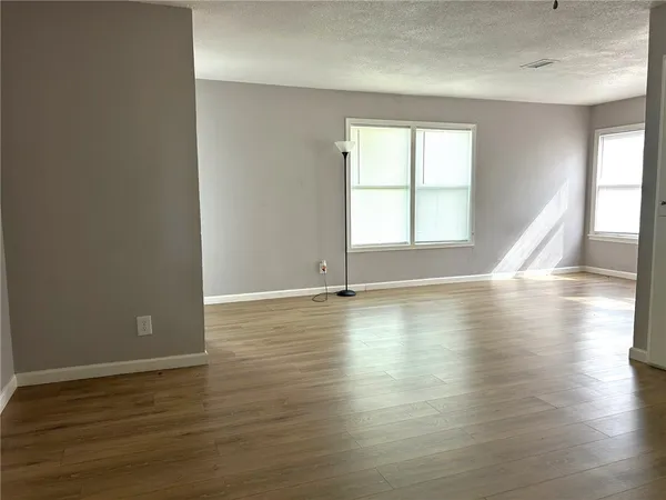 an empty room with wooden floor and windows with curtains