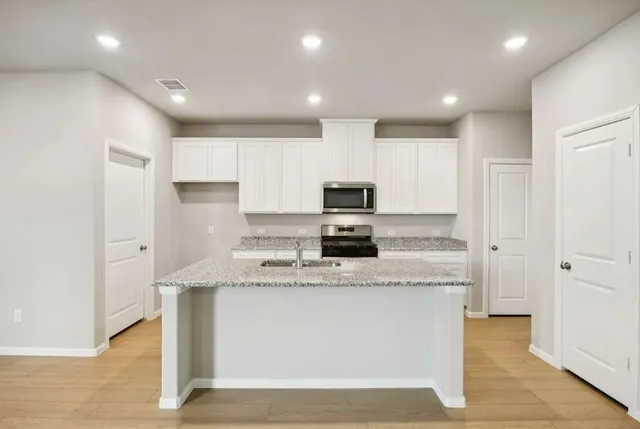 a large kitchen with stainless steel appliances granite countertop a stove a sink a refrigerator and white cabinets with wooden floor