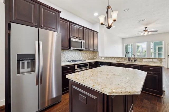 a kitchen with stainless steel appliances granite countertop wooden cabinets a sink dishwasher a stove and a large window with wooden floor