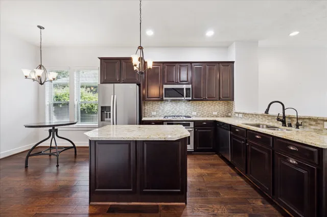 a kitchen with a stove a refrigerator a sink a dining table and chairs with wooden floor