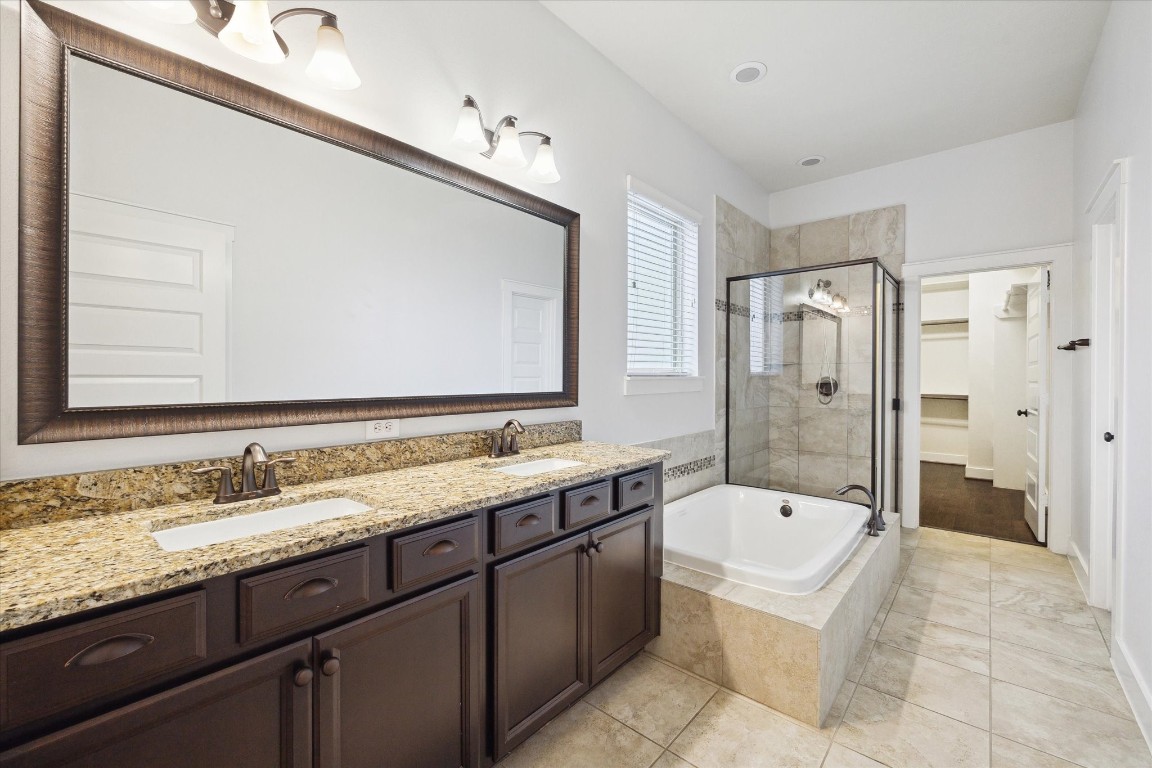 17011 Seminole Ridge Drive Cypress, TX 77433 - Photo 19 of 33 This bathroom features a double-sink vanity with granite countertops and dark wood cabinets. It includes a soaking tub with a glass-enclosed shower, tiled walls, and floor.