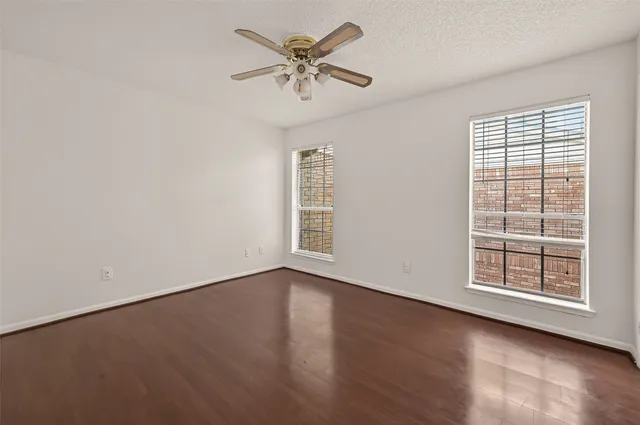 an empty room with wooden floor chandelier fan and windows