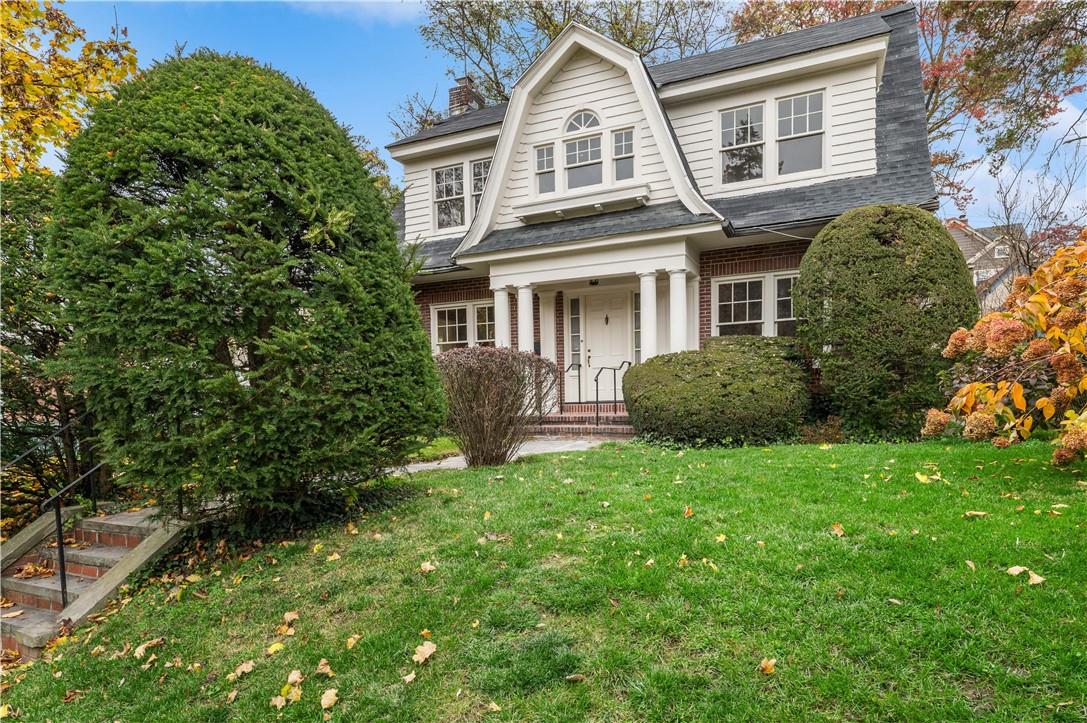 a view of a big yard in front of a brick house with plants and large trees