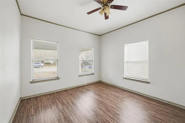 an empty room with wooden floor chandelier fan and windows