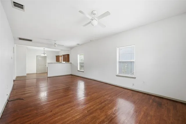 a view of a livingroom with wooden floor a ceiling fan and windows