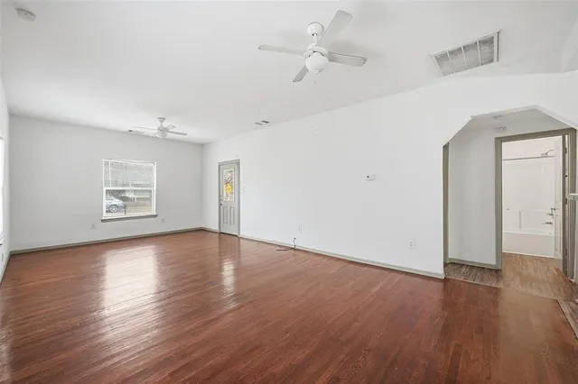 an empty room with wooden floor chandelier fan and windows
