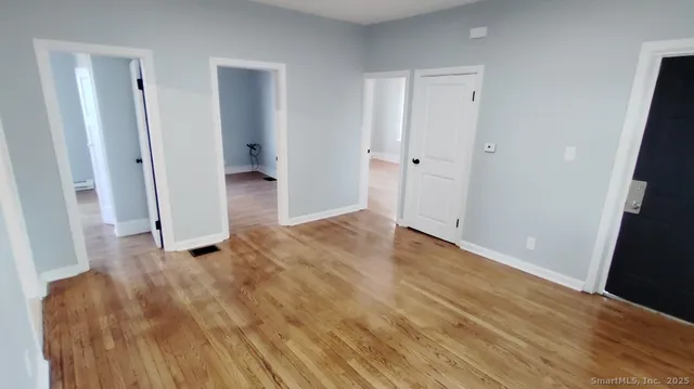 a view of an empty room with wooden floor and a bathroom