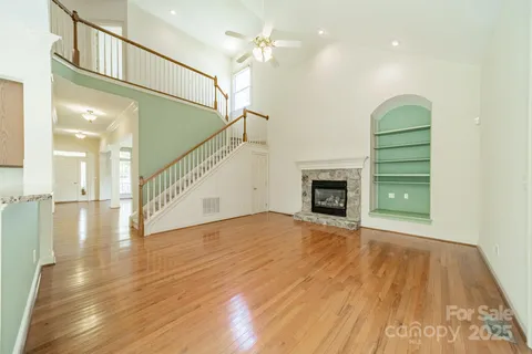 a view of an empty room with wooden floor a fireplace and a window