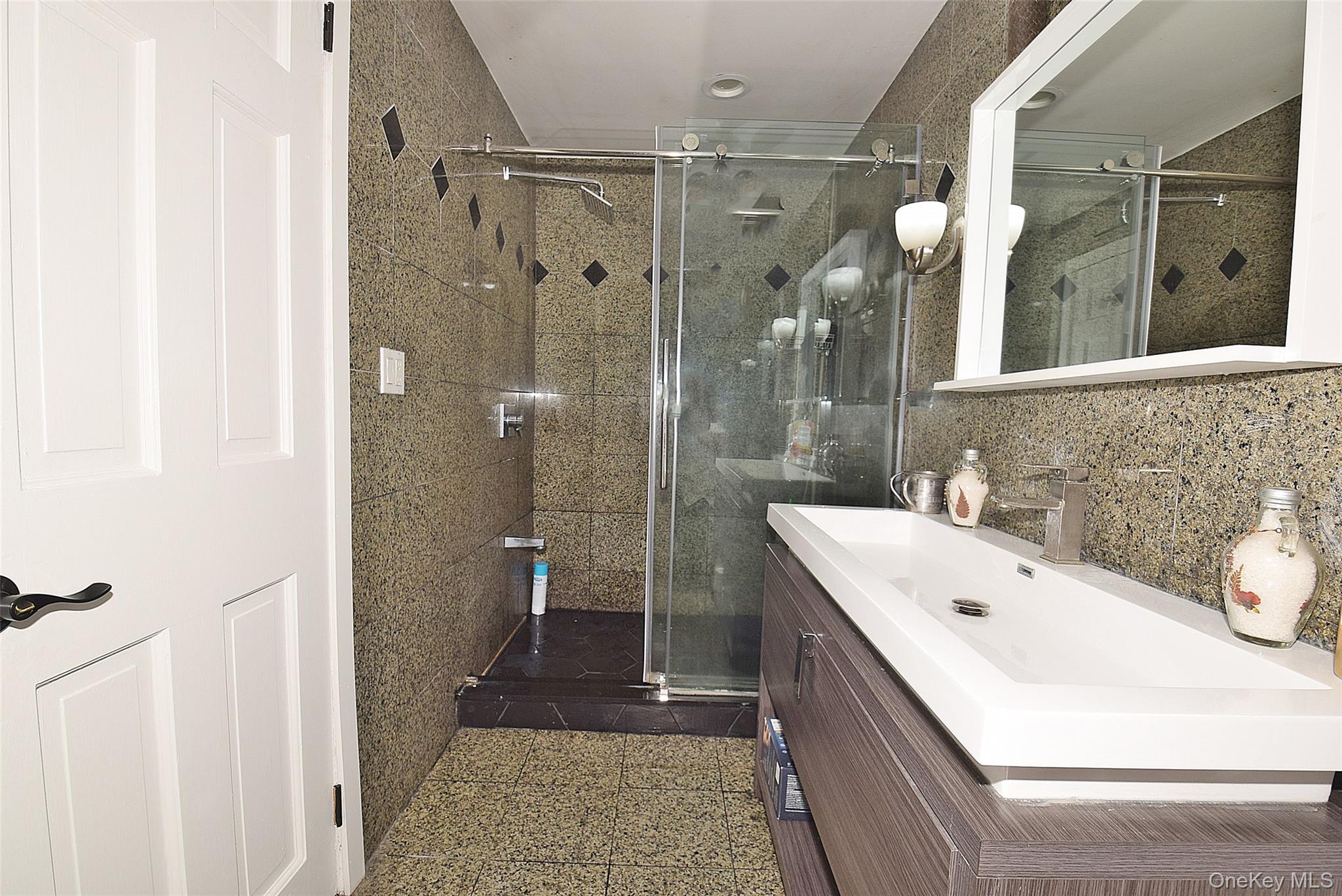 25 Old Mill Road Great Neck, NY 11023 - Photo 19 of 45 Floating vanity with integrated basin, brushed nickel faucet, mirrored medicine cabinet, and glass-enclosed shower with tile surround