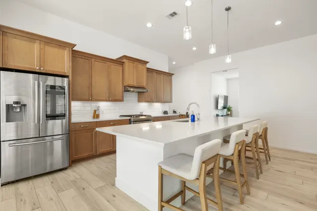 a kitchen with stainless steel appliances kitchen island granite countertop a refrigerator a stove a sink a dining table and chairs with wooden floor
