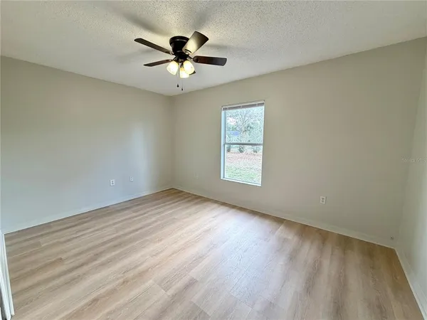 an empty room with wooden floor ceiling fan and window