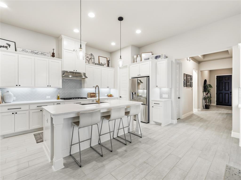 15340 Crape Myrtle Road Frisco, TX 75035 - Photo 5 of 40 Bright kitchen featuring white cabinetry, a large island with seating, stainless steel appliances, pendant lighting, and light wood-finish flooring