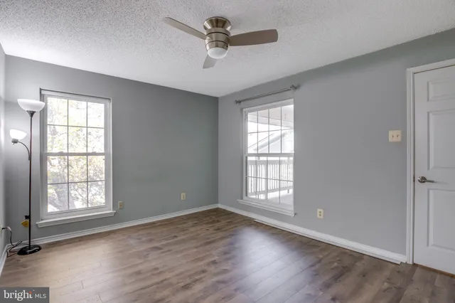 an empty room with wooden floor chandelier fan and windows
