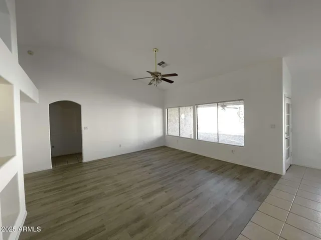an empty room with wooden floor a ceiling fan and windows
