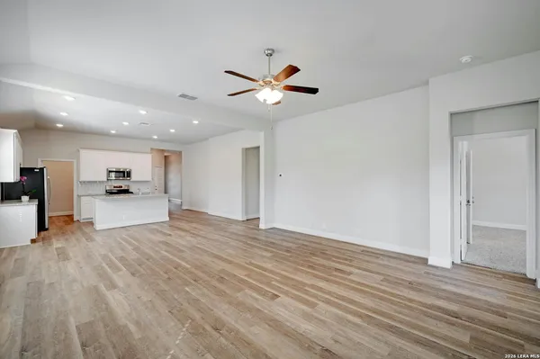 a view of an empty room with wooden floor and a ceiling fan