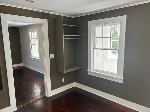 an empty room with wooden floor closet and windows