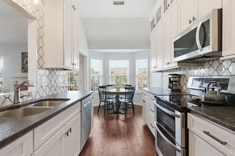 a kitchen with stainless steel appliances wooden floor sink stove dining table and chairs