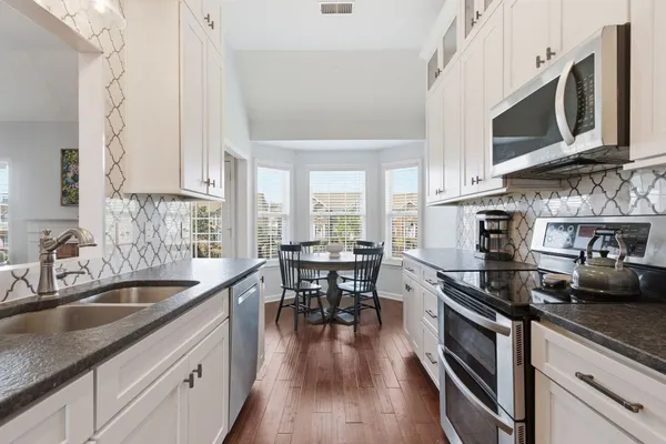 a kitchen with stainless steel appliances wooden floor sink stove dining table and chairs
