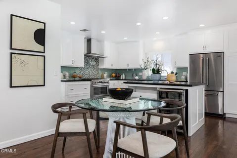 a kitchen with stainless steel appliances granite countertop a dining table chairs refrigerator and microwave