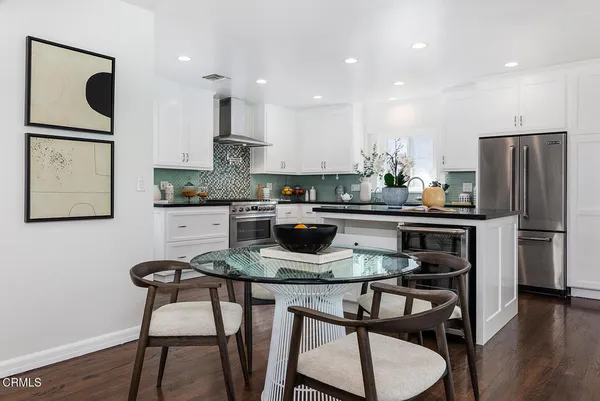 a kitchen with stainless steel appliances granite countertop a dining table chairs refrigerator and microwave