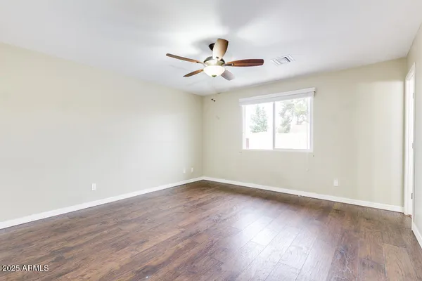 an empty room with wooden floor fan and windows
