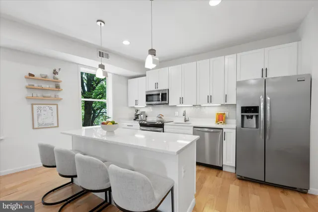 a kitchen with stainless steel appliances a stove a refrigerator a sink dishwasher a dining table and chairs with wooden floor