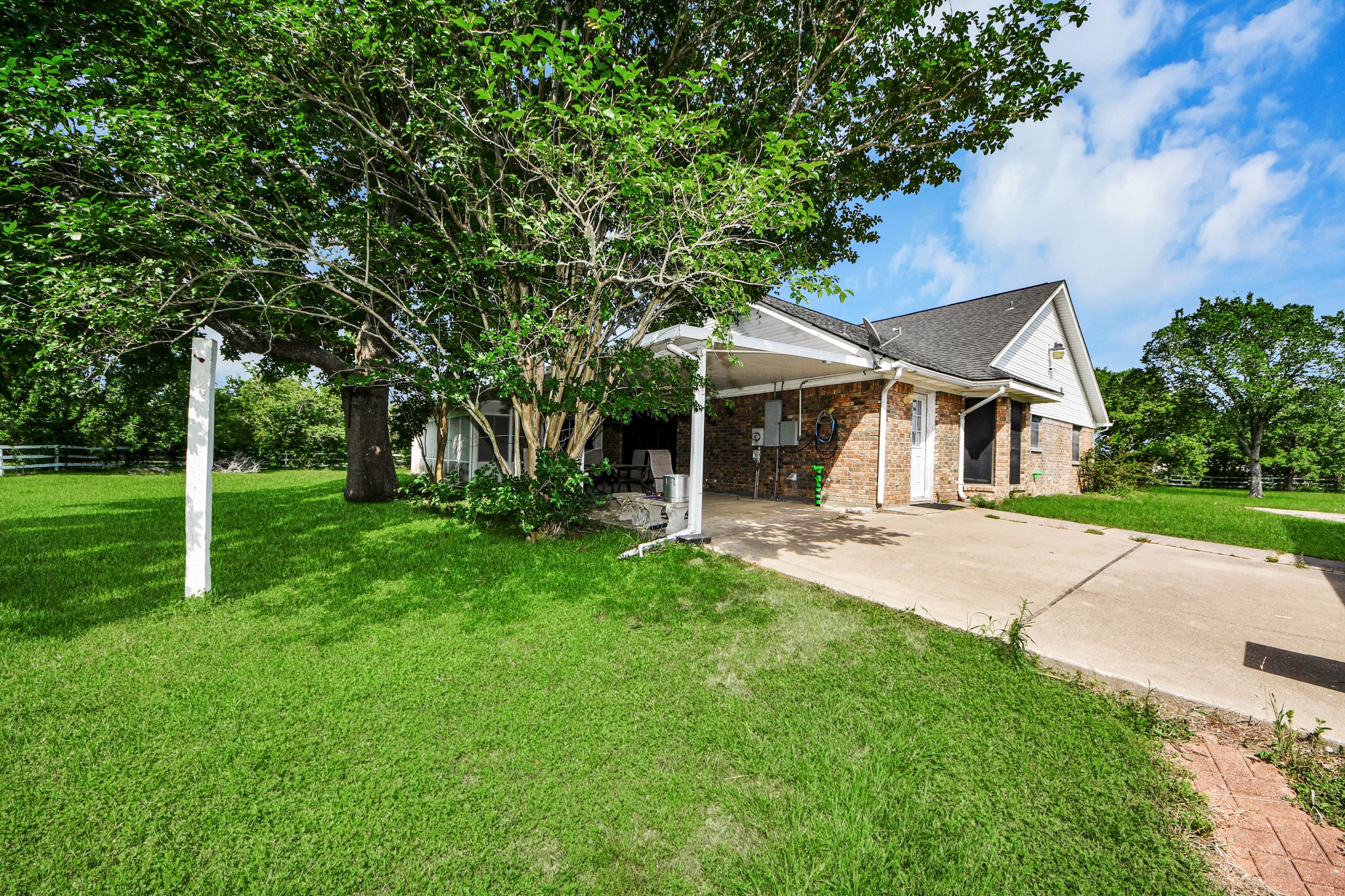 12746 Roy Road Pearland, TX 77581 - Photo 4 of 47 Charming brick house with a carport, surrounded by lush greenery and mature trees. The spacious yard offers ample space, perfect for outdoor activities or gardening.