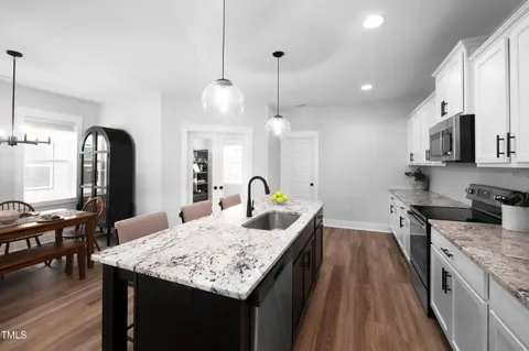 a large kitchen with granite countertop a stove a sink a center island and wooden floor